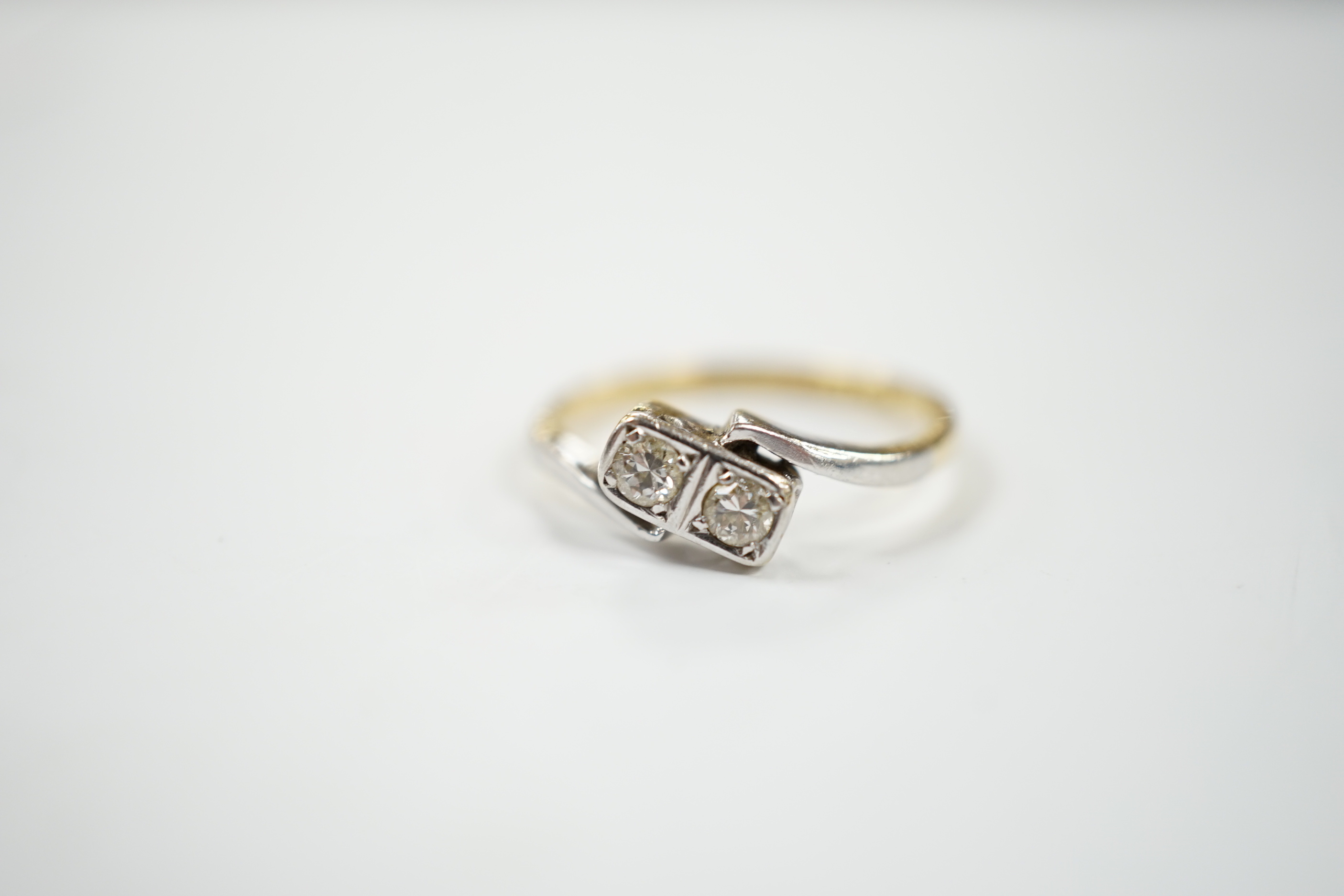 An 18ct, plat and two stone diamond set crossover ring, size M, gross weight 2.3 grams.